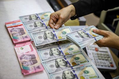 Seorang petugas menunjukan pecahan Dolar AS dan Rupiah di salah satu tempat penukaran mata uang asing di Kwitang, Jakarta, Senin (9/12/2024). Foto: Ist