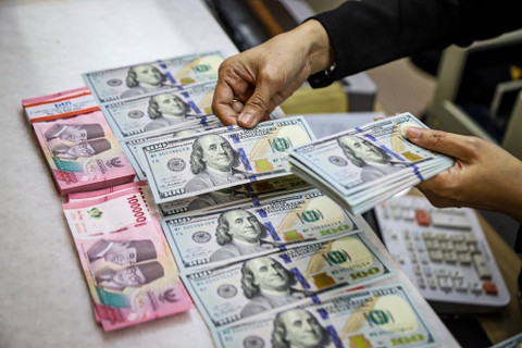 Seorang petugas menunjukan pecahan Dolar AS dan Rupiah di salah satu tempat penukaran mata uang asing di Kwitang, Jakarta, Senin (9/12/2024). Foto: kumparan